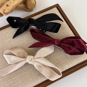 Three velvet bow hair clips in black, wine red, and cream on a textured fabric background
