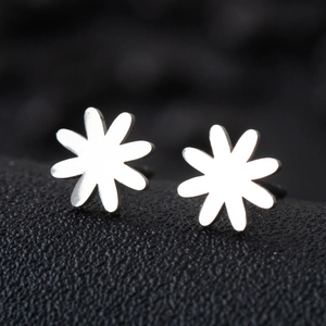 Macro shot of polished silver daisy flower stud earrings on black textured surface