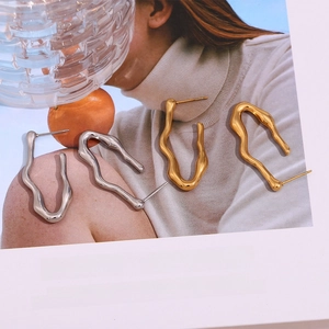 Detailed close-up of wavy gold and silver stainless steel earrings on a magazine page