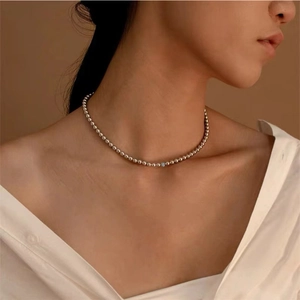 Minimalist silver beaded necklace with tiny blue gemstone on a model wearing white shirt