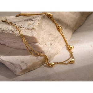 Close-up of double-layer gold heart anklet placed on a textured stone under sunlight