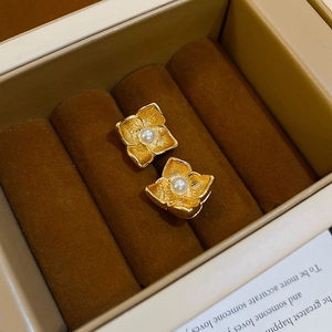 Nahaufnahme goldener Blumenohrringe mit weißen Perlen in einer braunen Samt-Box