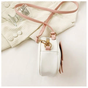Detail view of white round mini bag with pink strap showing stitching and metal clasp
