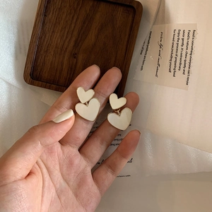 Close-up of cream double heart earrings with gold trim held by a hand over a tray