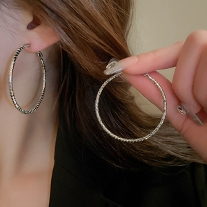 Close-up of large silver hoop earrings with geometric textured finish on female model