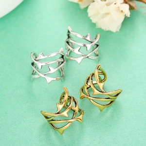 Dettaglio di ear cuff punk a forma di spine in oro e argento su sfondo verde