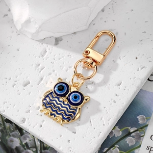 Golden owl keychain with blue evil eye accents on a white textured background