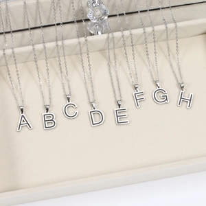 Minimalist stainless steel initial necklaces with silver letters A to H on a jewelry tray