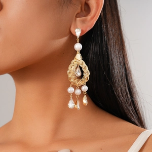 Detail view of gold hollow earrings featuring woven metal with pearls and drop crystals