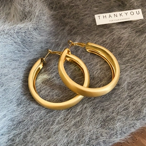 Macro shot of matte gold chunky hoop earrings with a brushed finish on plush gray fabric