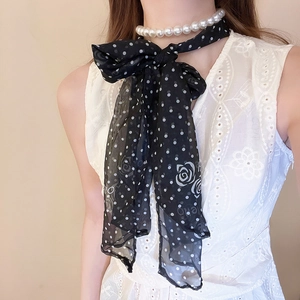 Detail of a black polka dot silk scarf with white roses and a pearl necklace
