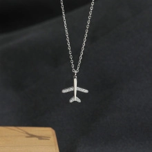 Macro detail of silver airplane necklace pendant with zircon wings on a dark surface