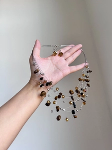 Detailed view of layered tiger eye stone necklace and matching earrings held in hand