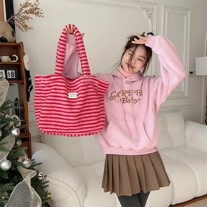 Detailed shot of pink and red striped plush tote bag with logo patch in home setting