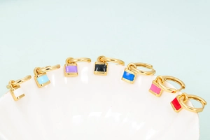 Macro shot of colorful drip oil padlock pendant earrings arranged on white shells
