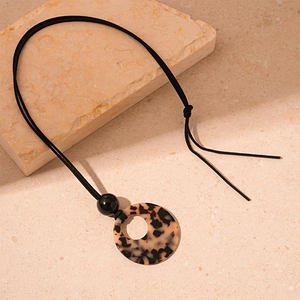 Detail of tortoiseshell acrylic ring pendant on a minimalist black rope sweater necklace