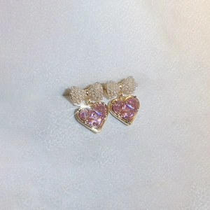 Dettaglio macro di orecchini a cuore placcati oro con gemme rosa e fiocco di perle