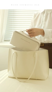 A person placing a cream PU leather makeup bag into a matching large tote bag near a window