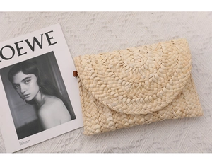 Dettaglio di pochette in paglia intrecciata con patta semicircolare e linguetta marrone