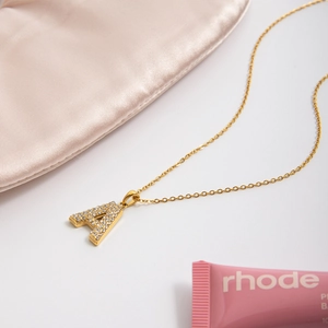 Close-up of golden letter A pendant with shimmering stones on elegant silk background