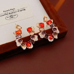 Macro shot of U-shaped gold earrings with colorful zircon stones on brown velvet