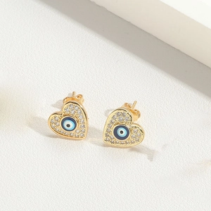 Detailed close-up of gold heart stud earrings featuring evil eye motif and crystals