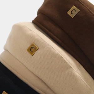 Close-up detail of soft autumn beret hats featuring a vintage bronze metal square with C logo