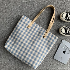Flache Ansicht der blau karierten Canvas-Tasche mit Ledergriffen und Lifestyle-Zubehör