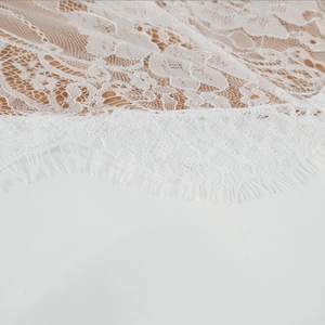 Close-up of white floral lace fabric featuring delicate eyelash fringe details