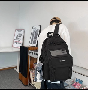 Vista posteriore di uno zaino in nylon nero capiente con tasche a rete e ciondolo