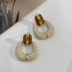 Detail view of retro gold-plated earrings with brown enamel and pearly C-shaped accents