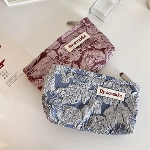 Detail of floral relief pattern on zippered cosmetic bags in grey-blue and pink colors