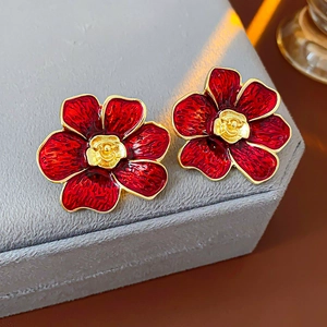 Detalle macro de pendientes de flores rojas vintage con borde metálico dorado en soporte