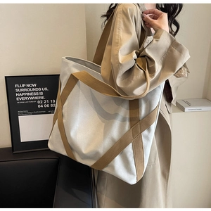 Detail of a large canvas tote bag with brown straps worn by a model in a minimal setting