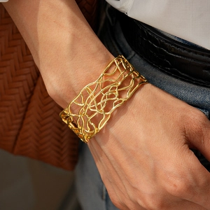 Close-up of golden wide mesh cuff bracelet on female wrist with casual outfit styling