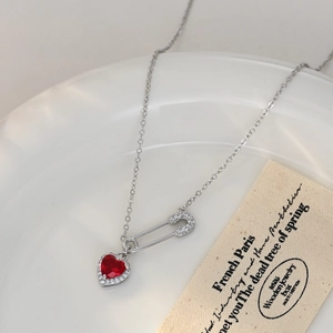 Detailed macro of a safety pin pendant and red heart gem on a fine silver chain