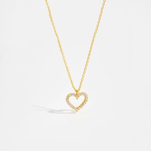 Macro shot of minimalist gold heart necklace with sparkling white zircons on white background