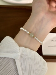 Detailed shot of a pearl bracelet featuring a light green jade centerpiece on a wrist