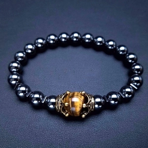 Dettaglio del bracciale con corona dorata, occhio di tigre e perle di ematite nera
