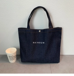 Detail of dark blue denim tote bag with white RAINBOW print and metal fastener detail