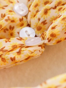 Dettaglio di un bottone bianco su abito giallo floreale che mostra la trama del tessuto