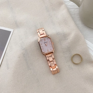 Detail of rose gold rectangular watch with light purple dial on textured fabric background