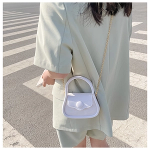 Mini white leather crossbody bag with gold chain strap shown in a street style view