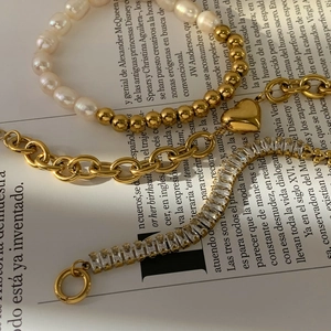 Close-up of stacked gold pearl bracelet set with heart pendant and zircon crystals