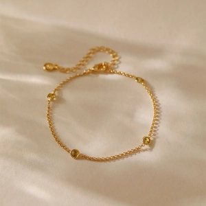 Detalle de pulsera de cadena dorada minimalista con tres gemas amarillas en tela beige