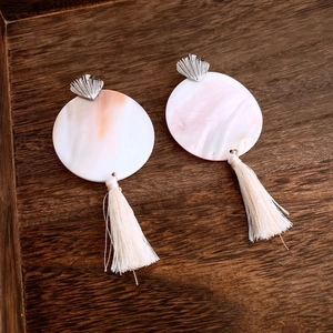 Detail of round shell fringe earrings with pink gradient on a dark wood tray