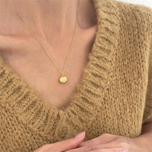 Detail of a gold-plated shell pendant necklace worn over a textured brown sweater