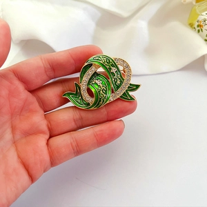 Vintage palace style green enamel brooch with gold leaves and crystals held against fabric