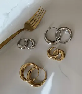 Detail von goldenen und silbernen Chunky Hoop Ohrringen in zwei Größen auf Marmorgrund