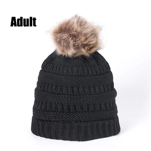 Detail of chunky knit winter beanie for adults with fluffy pom-pom in deep black